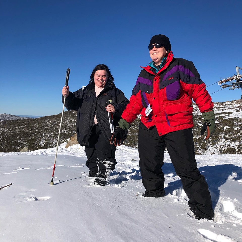 Two travelers with white canes walking in snow on a sunny day